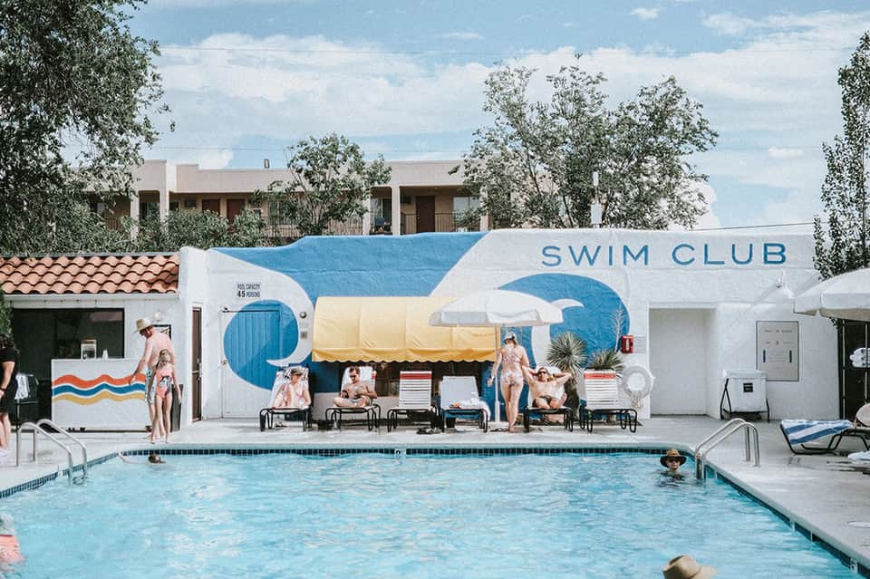 Retro swim club with blue and white mural, lounge chairs, and guests relaxing by the pool