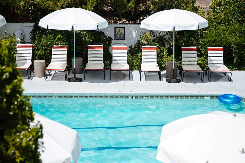 Resort pool area with striped lounge chairs, white umbrellas, and palm trees