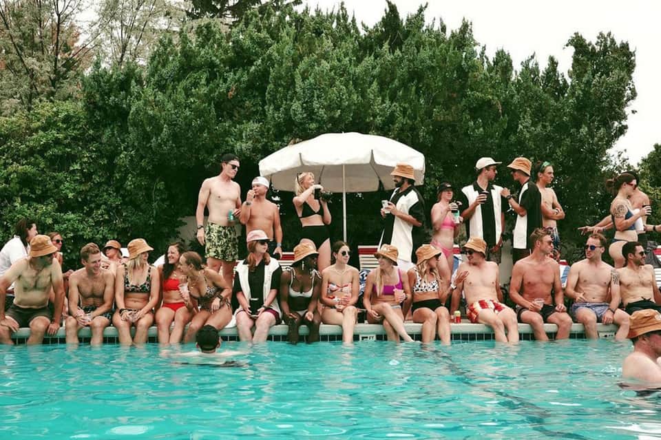 Large group of guests in straw hats relaxing poolside under white umbrellas at resort