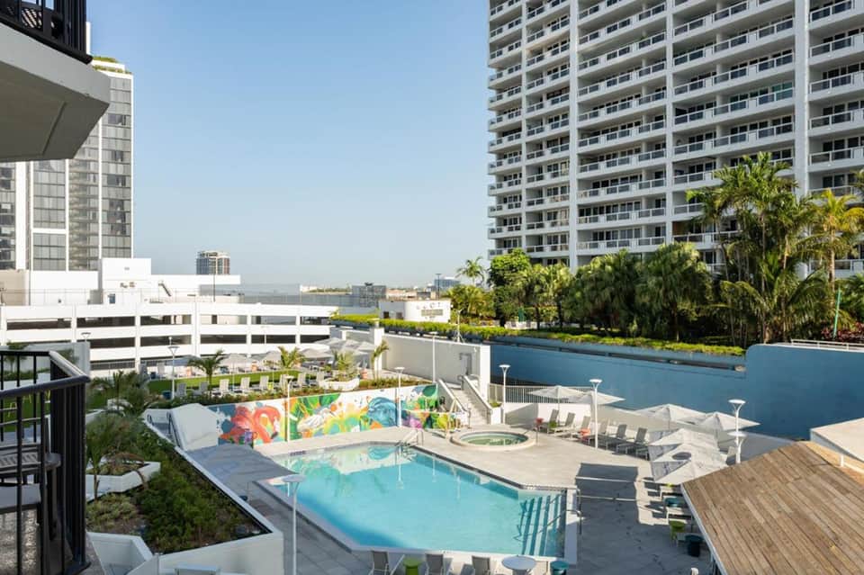 Modern resort pool with colorful mural, loungers, and high-rise buildings surrounding the urban rooftop terrace