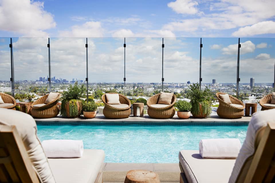 Luxury rooftop pool with woven lounge chairs and city skyline views behind glass barriers