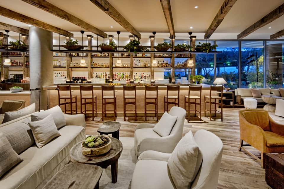 Modern bar and lounge area with wooden beams, exposed ceiling, bar seating, and large windows overlooking landscape