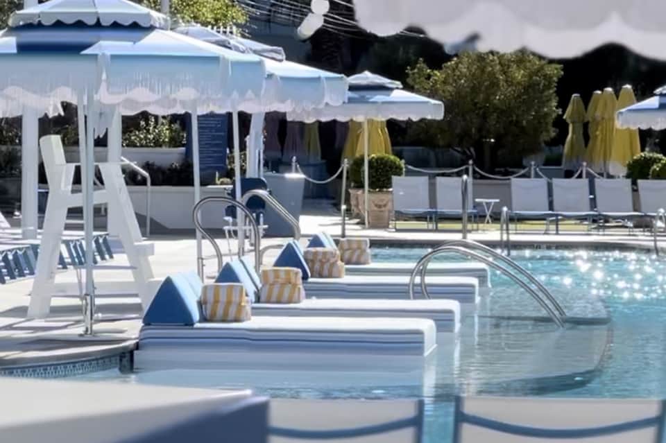 Luxurious resort pool with white cabanas, umbrellas, and lounge chairs on sunny day
