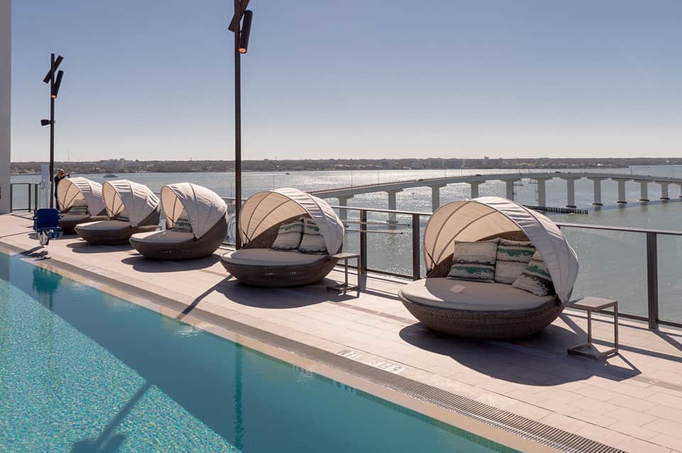 Resort rooftop lounge with canopied daybed chairs overlooking a bay and bridge spanning the water