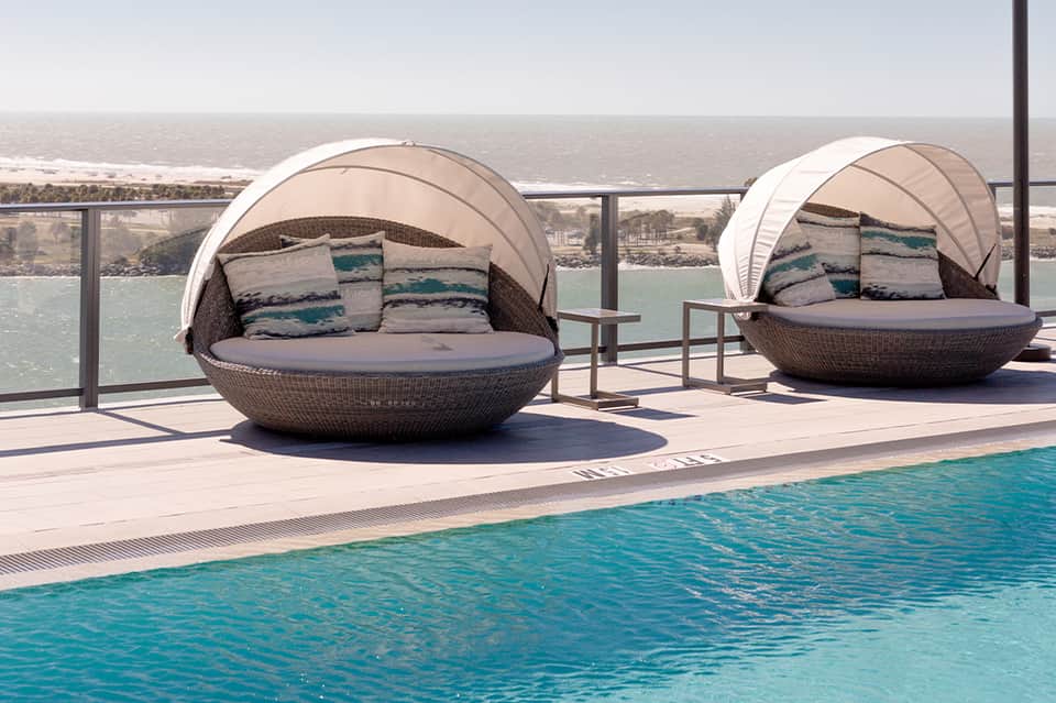 Two woven pod loungers with cushions on infinity pool deck overlooking water