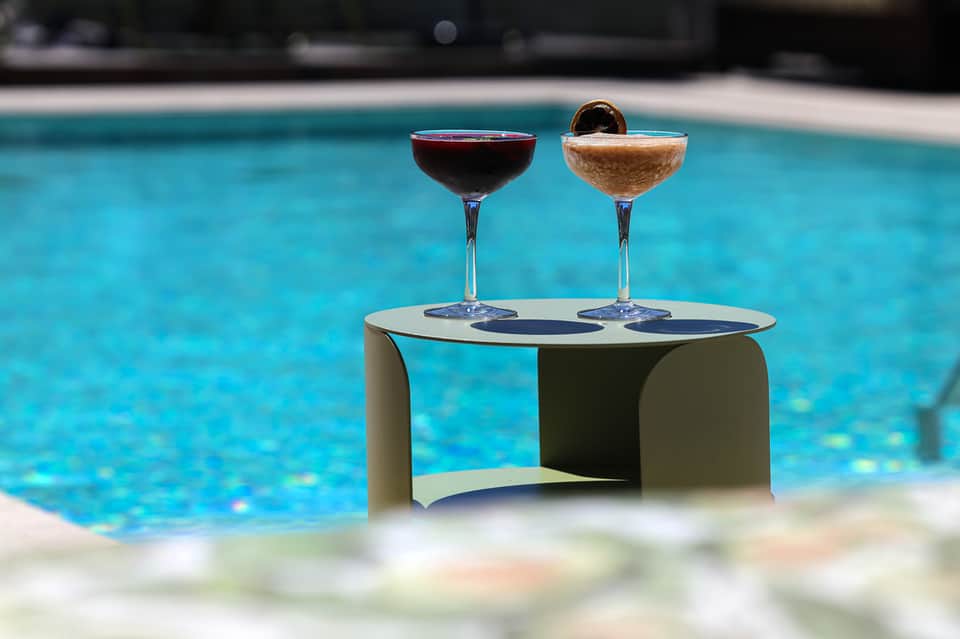 Two elegant cocktails on a white table beside a turquoise swimming pool