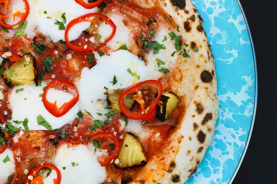 Gourmet pizza with fresh mozzarella, red peppers, pineapple, and herbs on blue plate