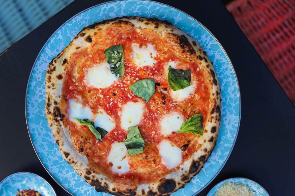 Margherita pizza with fresh basil on blue plate, traditional wood-fired preparation with charred crust