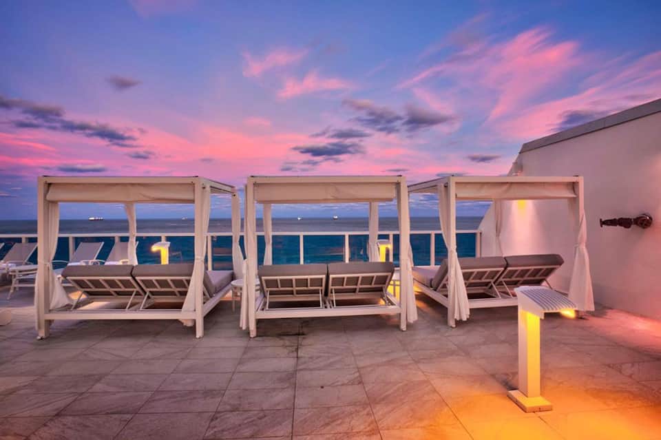 Beachfront cabana beds with ocean view at sunset with pink and purple sky