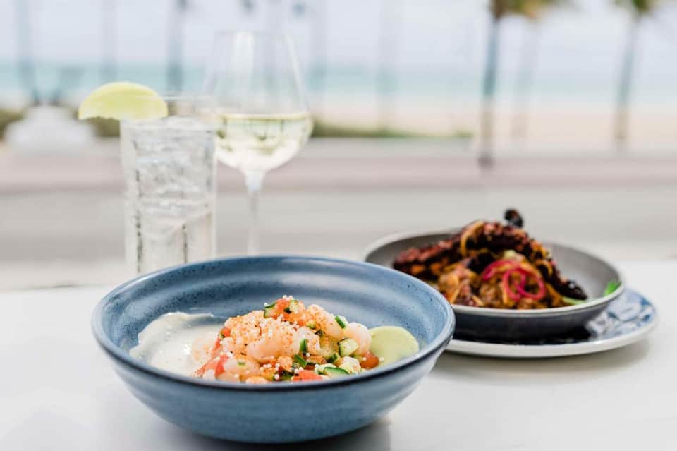 Fine dining plate with shrimp dish and cocktails on outdoor waterfront terrace