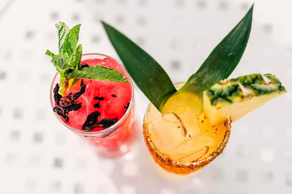 Two tropical cocktails with fresh mint and pineapple garnish on white surface