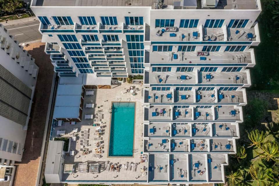 Aerial view of resort with multiple pool decks, blue swimming pool, and white modern building
