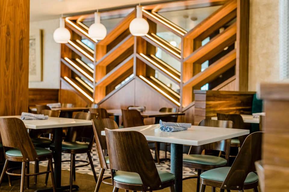 Modern restaurant interior with wooden chevron ceiling design, pendant lights, and dining tables