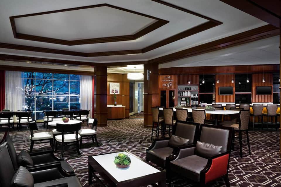 Upscale hotel lounge with dark wood ceiling, leather seating, bar area, and panoramic windows