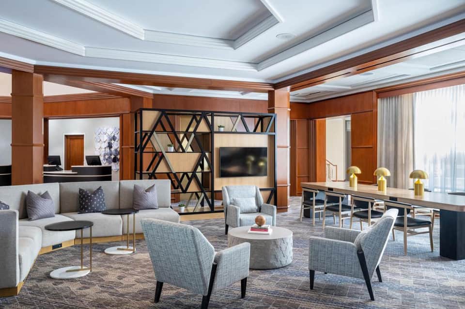 Luxury hotel suite lounge with coffered ceiling, gray sectional sofa, modern fireplace divider, and dining area