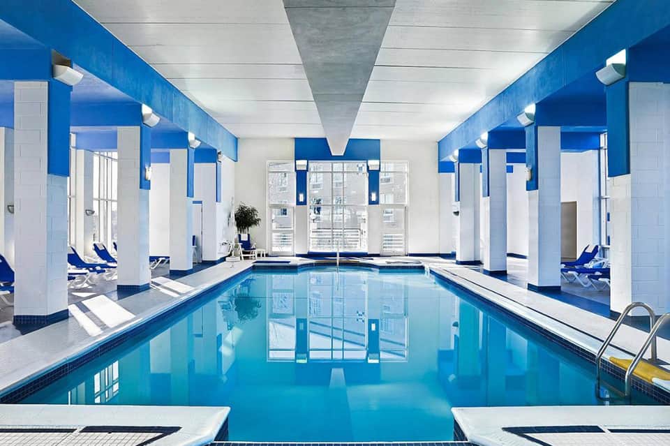 Indoor lap pool with blue and white striped walls, white columns, and lounge chairs