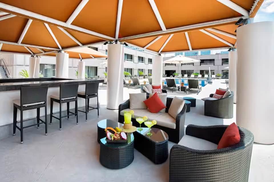Rooftop lounge area with orange umbrellas, black wicker seating, bar counter, and city views