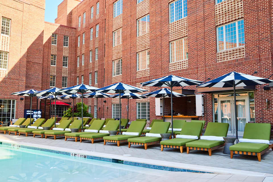 Brick courtyard pool area with lime-green lounge chairs, blue and white striped umbrellas, and historic brick buildings
