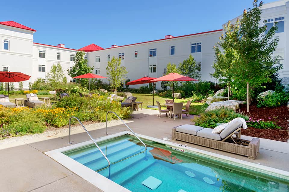Outdoor courtyard with swimming pool, red umbrellas, lounge chairs, and white hotel building with red roof