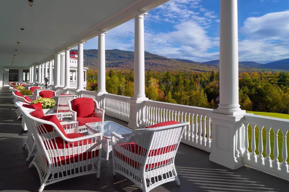 Mountain view from white columned porch with red cushioned wicker chairs and autumn forest