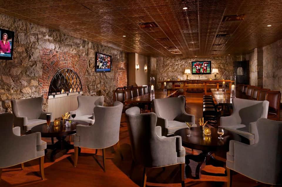 Upscale lounge with exposed brick walls, gray wingback chairs, wooden bar, and flat-screen TVs