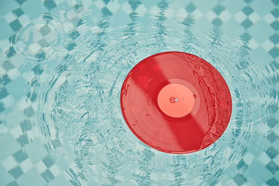 Red floating device creating ripples in a turquoise swimming pool with diamond pattern tiles