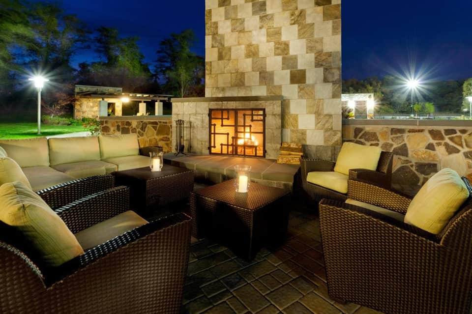 Outdoor patio seating area at night with wicker furniture, stone fireplace, and illuminated architecture