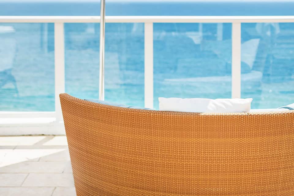 Orange wicker lounge chair on beachfront terrace with ocean view through glass railing