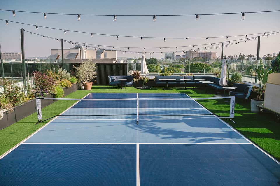 Rooftop pickleball courts with blue playing surfaces, lounge seating, and city views