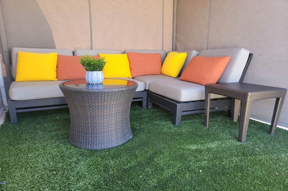 Modern outdoor seating area with gray sectional sofa, yellow and orange cushions, woven side tables, and artificial turf flooring