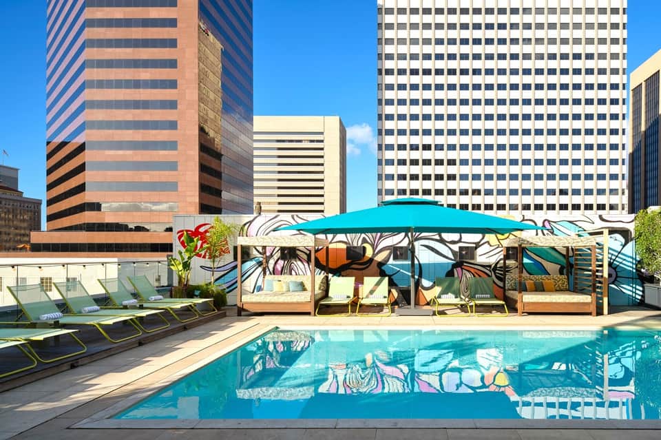 Rooftop pool with turquoise water and colorful mural, surrounded by lounge chairs and modern skyscrapers