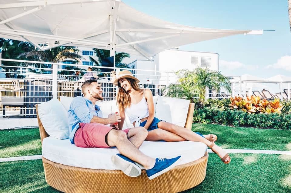 Couple relaxing on round lounge chair under white umbrella with tropical resort in background