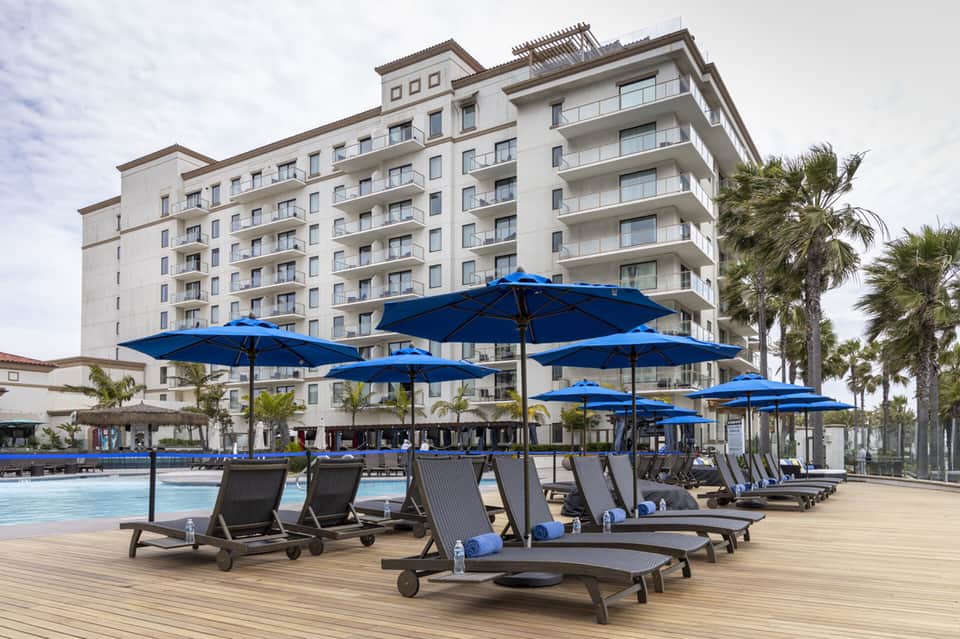 Multi-story beachfront hotel with blue umbrellas over lounge chairs on wooden deck