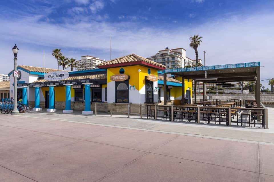 Colorful beachfront restaurant with blue columns, yellow building, and outdoor seating area