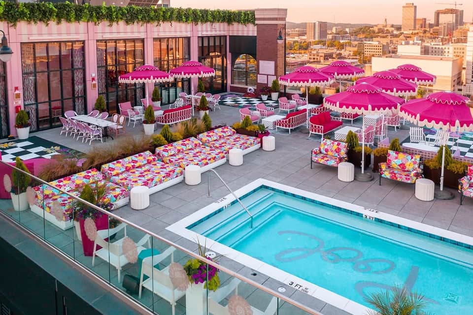 Rooftop pool area with vibrant pink umbrellas, lounge chairs, colorful cushions, and pink building facade