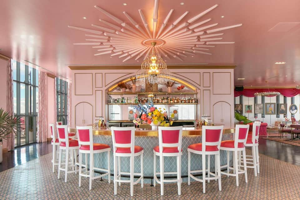 Elegant pink bar with white chairs, crystal chandelier, and colorful floral arrangement