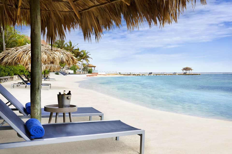 Tropical beach resort with thatched roof cabanas, lounge chairs, and turquoise ocean waters