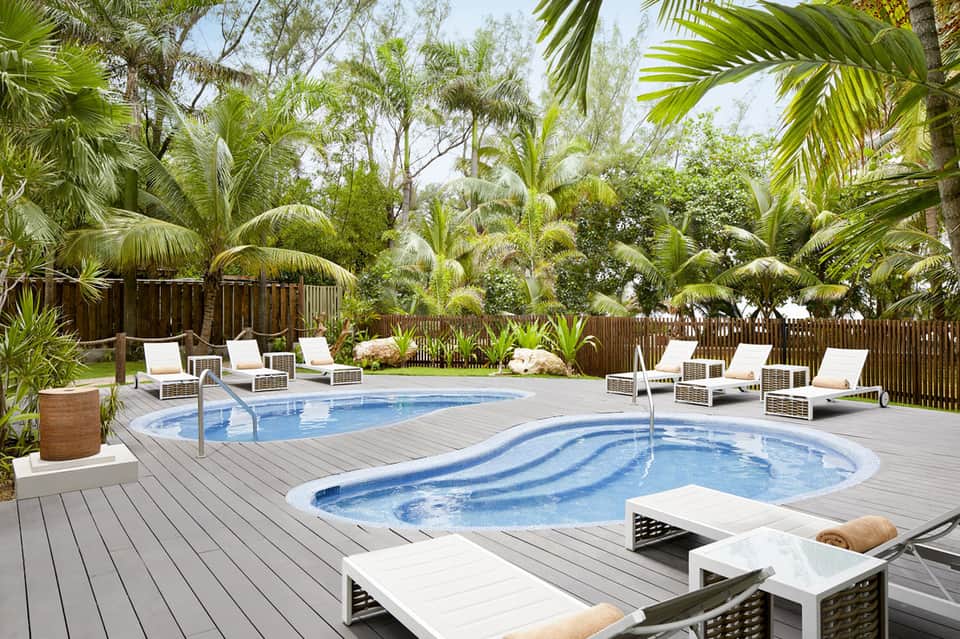 Resort pool surrounded by lush tropical palm trees with white lounge chairs on wooden deck