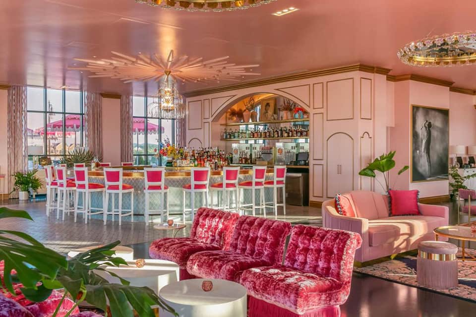 Luxurious pink lounge with velvet furniture, bar seating, crystal chandeliers, and ocean views through large windows