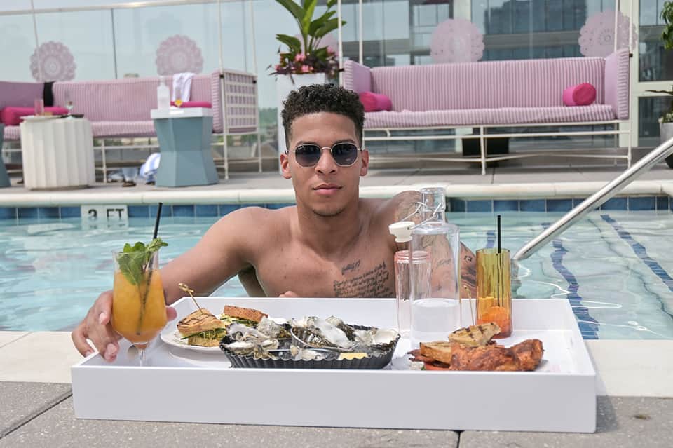 Man at resort pool holding tropical cocktail with oysters and seafood on white table