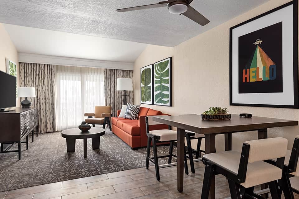 Modern hotel suite with orange sofa, dining table, and contemporary artwork on beige walls