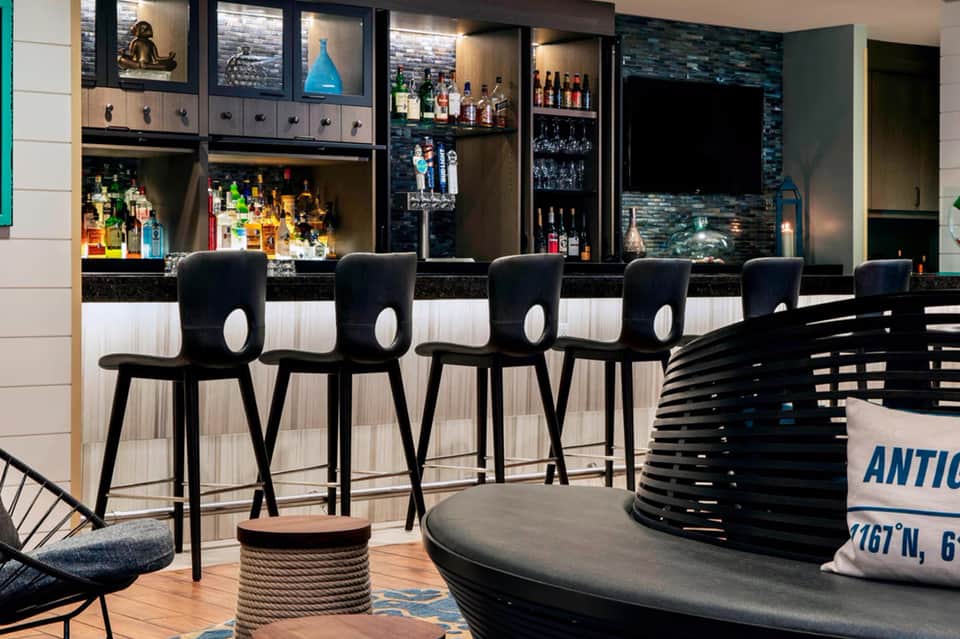 Modern hotel bar with black bar stools, illuminated liquor shelves, and contemporary lounge seating