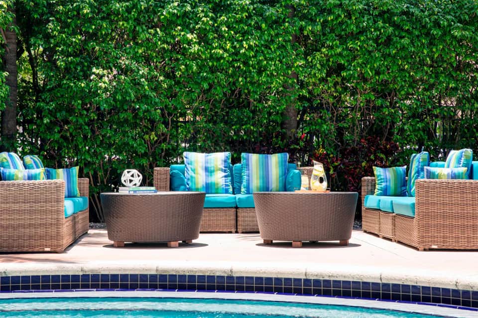 Woven lounge chairs with striped blue cushions arranged poolside behind a sparkling blue pool with lush green foliage backdrop