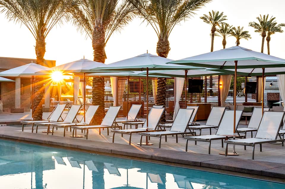 Luxury resort pool deck at sunset with lounge chairs, umbrellas, and palm trees