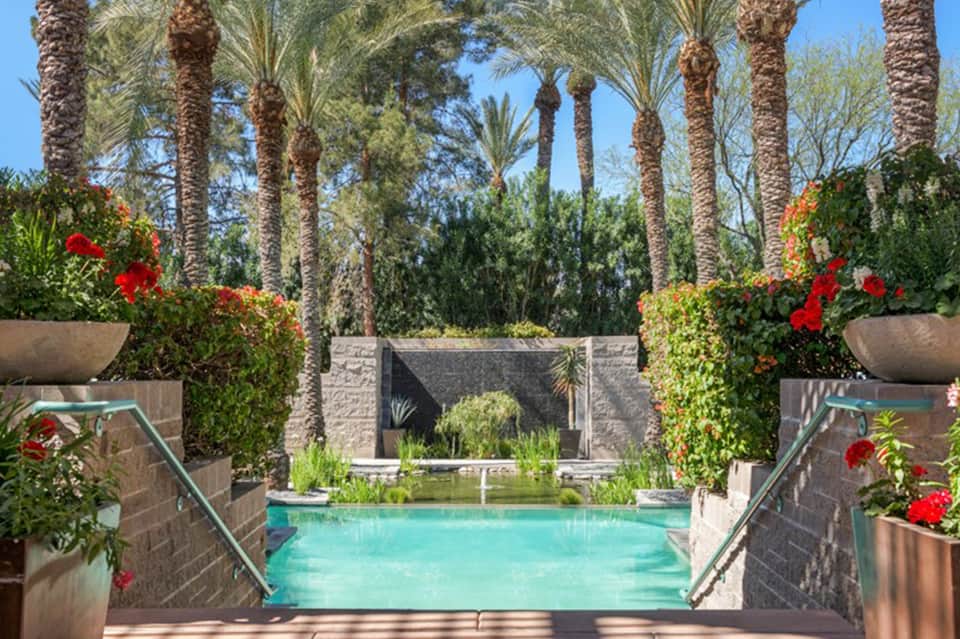 Turquoise pool framed by palm trees and red flowers in desert resort setting