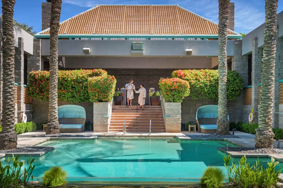 Luxury resort pool courtyard with turquoise water, palm trees, and Spanish colonial architecture with terracotta roof