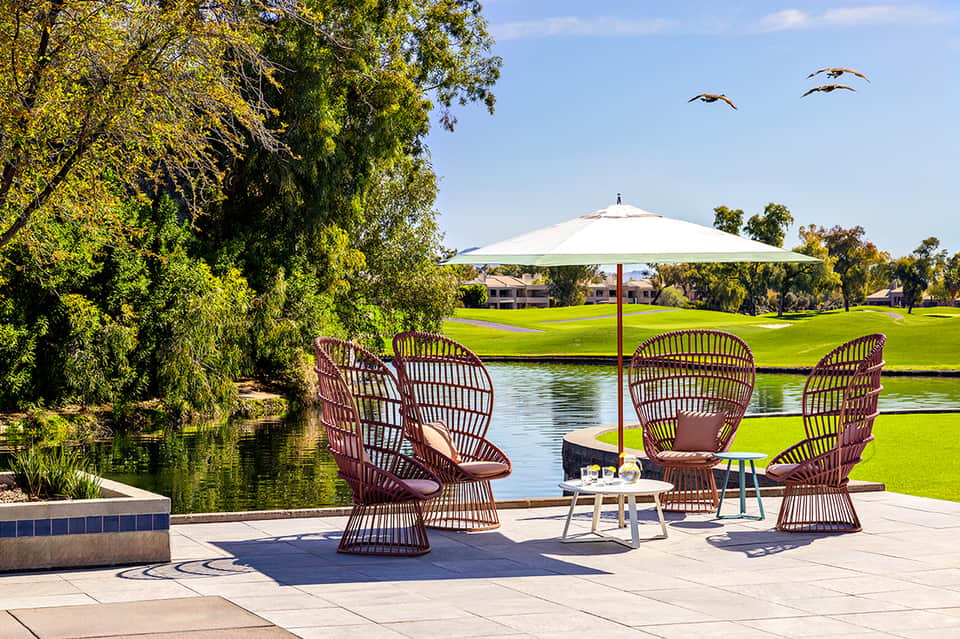 Modern rattan chairs with umbrella overlooking manicured lawn and calm pond water