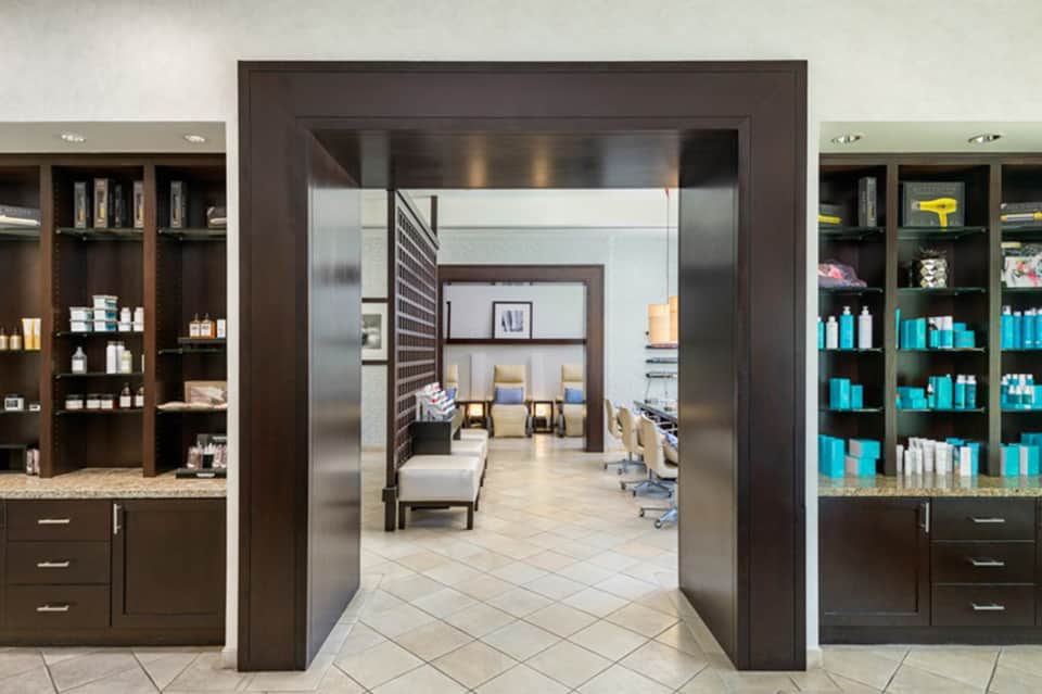 Spa salon interior with dark wood cabinetry, shelving displaying beauty products, and a doorway leading to treatment rooms