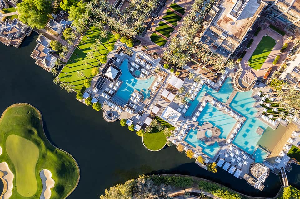 Aerial view of luxury resort with multiple pools, palm trees, and waterfront location