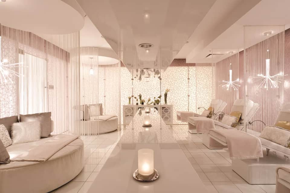 Luxurious spa lounge with pink tones, curved seating, decorative screens, and hanging crystal light fixtures
